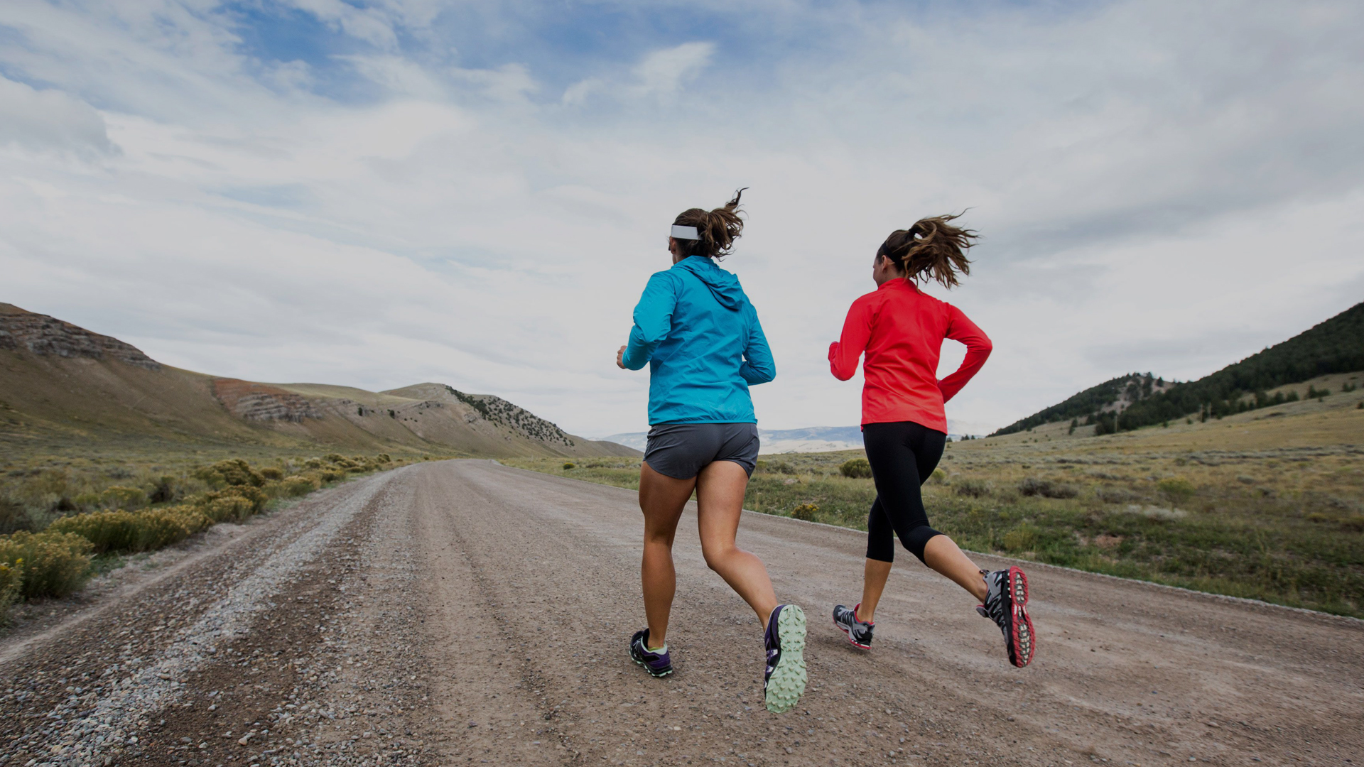 two people running on a road between hills